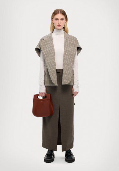 Szürke kockás mellény, fehér magasnyakú pulóver, barna szoknya elöl hasítékkal, sötétbarna kézitáska a kezében, fekete vastag talpú cipők.