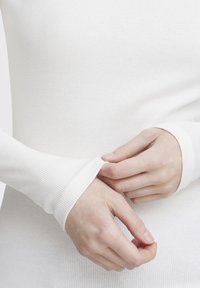 Hvit ribbete langermet topp med tettsittende mansjetter. Stoffet ser mykt ut med en lett tekstur som fremhever kroppens form.