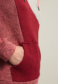Felpa con cappuccio rossa e rosa caratterizzata da un design testurizzato, tasca a marsupio e cappuccio regolabile con un pannello grigio a contrasto sulla parte superiore.