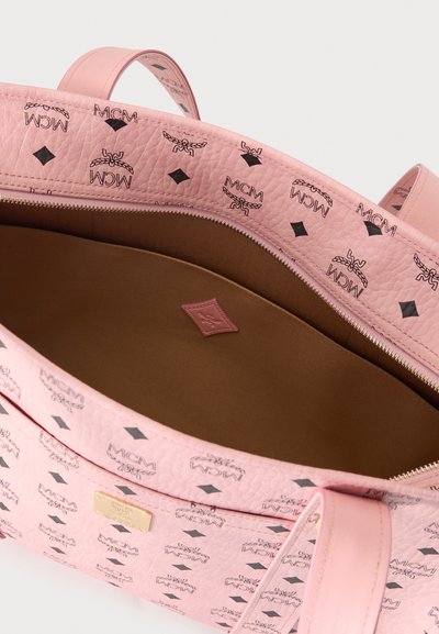 Sac à main en cuir rose avec logos MCM noirs, plaque dorée, ouverture zippée et doublure intérieure en tissu marron visible.