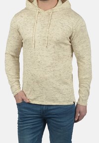 Hellbeige Kapuzensweatshirt aus weichem, strukturiertem Stoff mit einem dezenten, gesprenkelten Muster; verfügt über Kordeln und einen lässigen Schnitt.