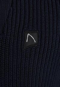 Temno moder pleten material z teksturiranim žabastim vzorcem, s črnim pravokotnim logotipom, na katerem je prikazan bel grafični element.