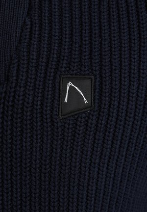 Tamno plavi pleteni materijal s teksturiranim rebrastim uzorkom, s crnim pravokutnim logotipom na kojem se nalazi bijeli grafički element.