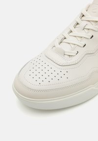 Vita lädersneakers med perforerad tåkappa, texturerad paneldesign, platta snören och gummisula. Minimalistisk och modern stil.