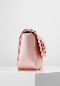 Růžová kožená kabelka s hladkým povrchem, se zlatým řetízkovým popruhem, bočním detailem ve tvaru mašle a strukturovaným obdélníkovým tvarem.