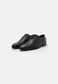 Pantofi din piele neagră, cu textură netedă, vârful ascuțit și cinci găuri pentru șireturi. Toc jos, plat și detalii de design minime.