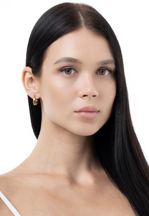 Goldene hoop Ohrringe an einem Model mit langen, glatten, dunklen Haaren und einem makellosen Teint; minimales Make-up, das die natürlichen Merkmale betont.