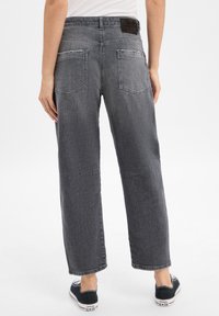 Jeans en denim gris avec une coupe droite, présentant des coutures visibles, deux poches arrière et une étiquette en cuir sur la ceinture.