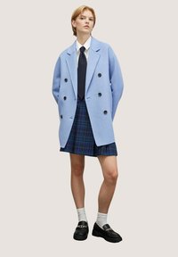 Lyseblå dobbeltrækker frakke, marineblå slips, hvid skjorte, plaid mini-nederdel, knæhøje hvide strømper og sorte loafers med kæde-detaljer.