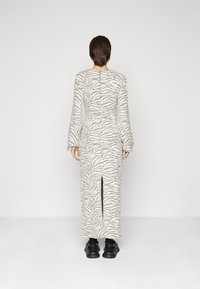 Długa, dopasowana sukienka w wzór zebry w kolorze białym i szarym. Posiada długie rękawy i rozcięcie z tyłu, dopełniona czarnymi butami.