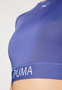 Sujetador deportivo morado con escote redondo y logotipo de PUMA en la banda elástica. Hecho de una tela suave y elástica con un diseño elegante.