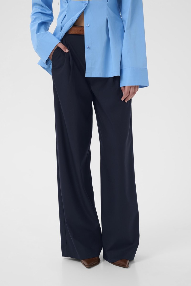 Ανοιχτό μπλε πουκάμισο με κουμπιά και χαλαρή εφαρμογή, σε συνδυασμό με σκούρο μπλε παντελόνι φαρδιάς γραμμής. Ορατή καφέ ζώνη, καφέ μυτερά παπούτσια ολοκληρώνουν το σύνολο.