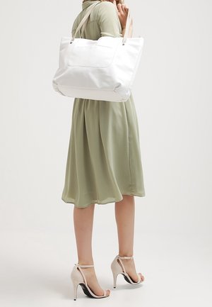 Sac fourre-tout blanc avec des poignées doubles, texture lisse, grand compartiment principal et pochette extérieure. Associé à une robe verte à mi-longueur.