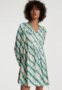 Langärmliges Kleid aus cremefarbener Baumwolle mit einem türkisfarbenen Batikmuster, V-Ausschnitt, gerafftem Bund und plissierten Details an den Ärmeln.