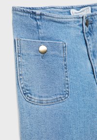 Jean en denim bleu clair en gros plan montrant une poche avant avec un bouton en métal et des détails de couture visibles.