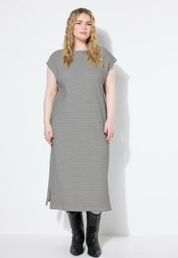 Gestreiftes Maxikleid aus schwarz-weißen Stoff mit kurzen Ärmeln, lockerer Passform und seitlichen Schlitzen. Kombiniert mit schwarzen, mit Nieten besetzten Stiefeln bis zum Knie.