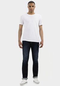 Witte short-sleeve t-shirt gecombineerd met donkerblauwe jeans en witte sneakers. De outfit heeft een relaxte pasvorm en een minimalistisch ontwerp.