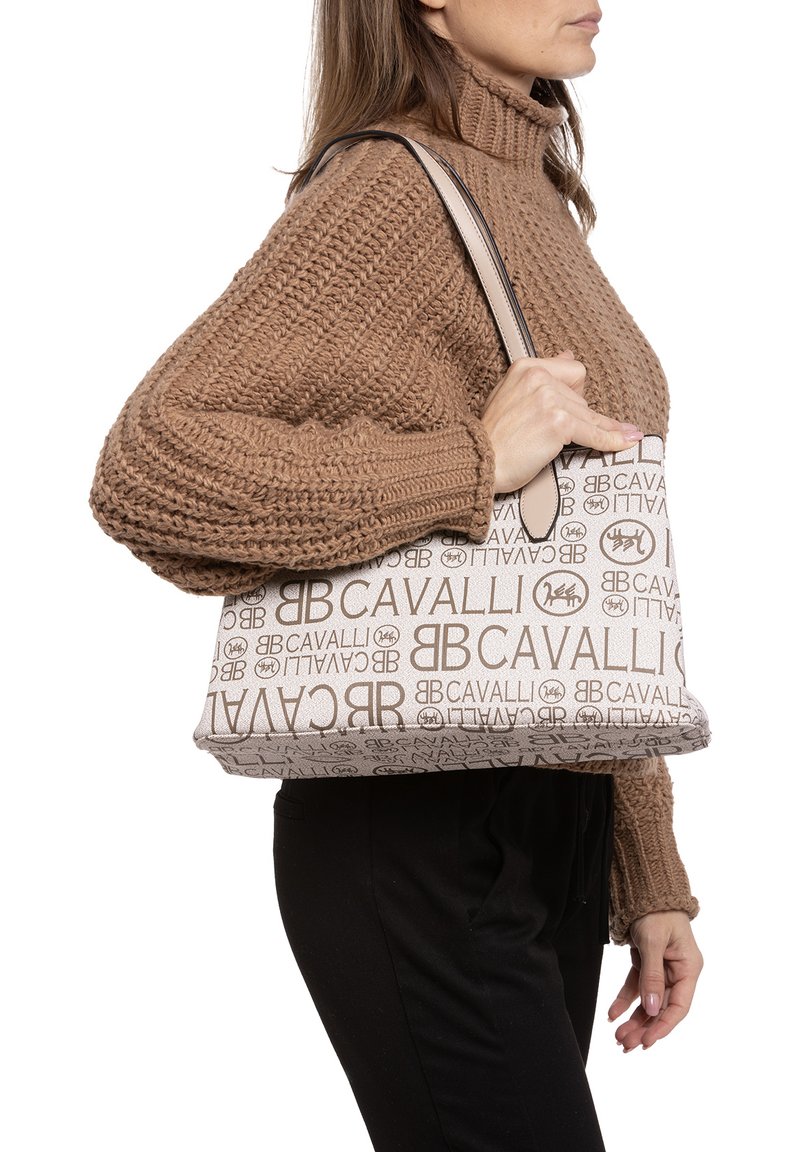 Sac à main beige avec un imprimé "CAVALLI" en marron sur l'ensemble. Le sac a une forme structurée avec une finition lisse et deux poignées.
