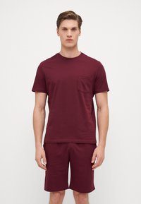 Burgundy cotton t-shirt with short sleeves and a chest pocket, paired with matching shorts, both in a smooth, lightweight fabric.