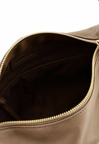 Interno di una borsa in pelle marrone con una cerniera dorata, caratterizzato da un rivestimento scuro e una piccola tasca con cerniera. Etichetta del brand visibile all'interno.