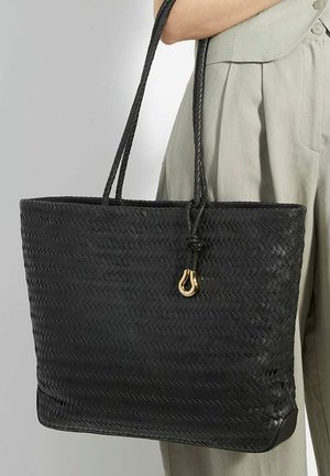 Black woven tote bag with thick, braided handles and a gold accent. Boxy shape with a textured finish and a flat base.