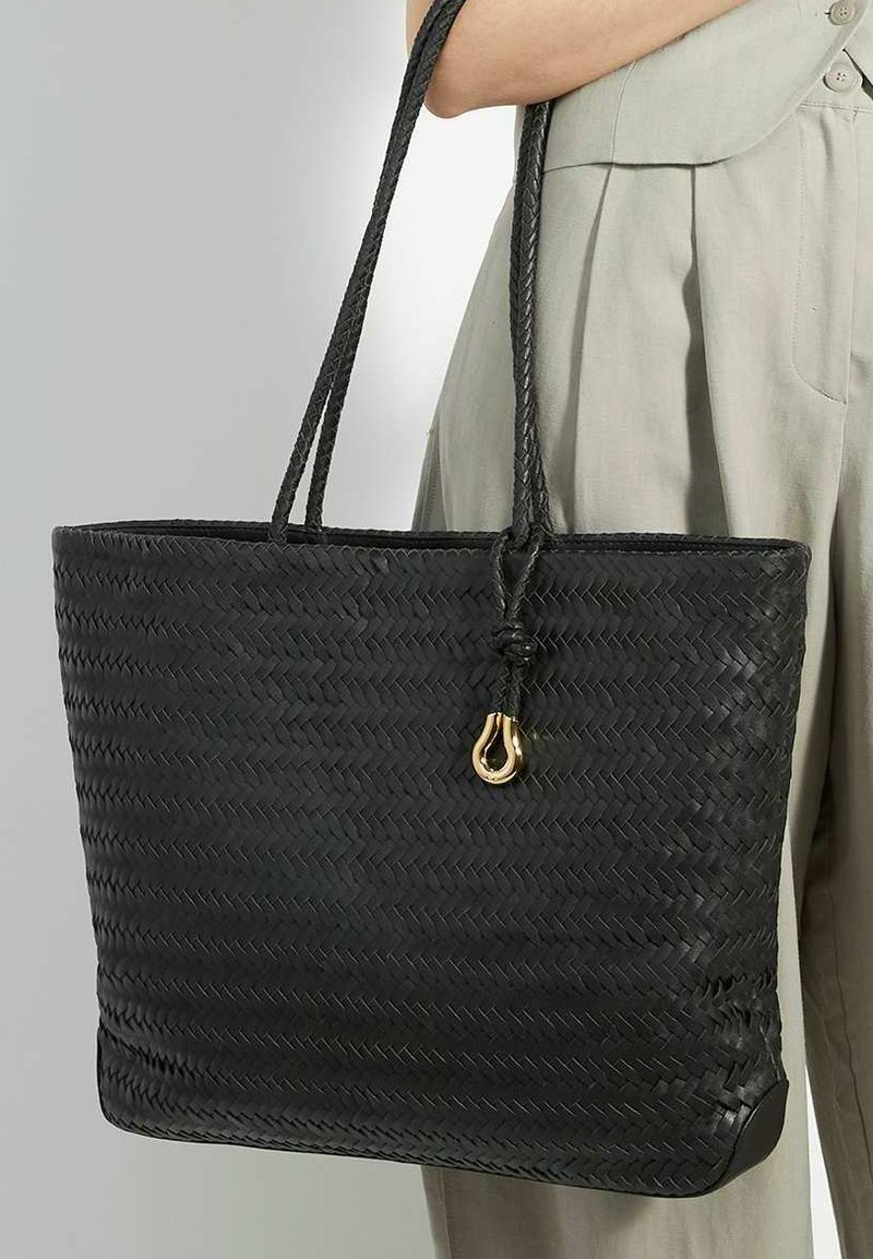 Black woven tote bag with thick, braided handles and a gold accent. Boxy shape with a textured finish and a flat base.