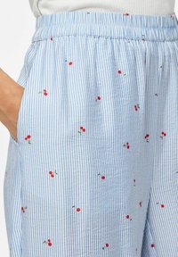 Pantalon rayé bleu clair avec broderies de cerises rouges. Le design comprend une taille élastique et des poches latérales, confectionné dans un tissu doux.