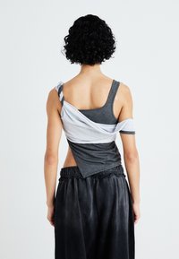 Top gris sin mangas con acento de tela blanca retorcida, diseño en capas y un ajuste corto. Combinado con pantalones de chándal oscuros y holgados.