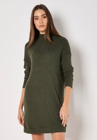 Robe en tricot côtelé vert avec des manches longues et un col montant, présentant une coupe décontractée et une longueur juste au-dessus du genou.