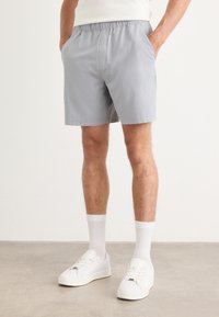 Grå shorts med elastisk linning, sidelommer og en avslappet passform, kombinert med hvite joggesko og knelange hvite sokker.
