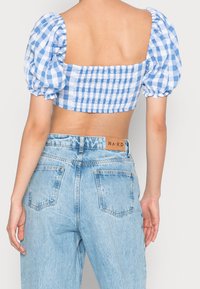 Blå og hvid ternet cropped top med puffede ærmer og smocked ryg, parret med lyseblå high-waisted denim jeans med et mærke.