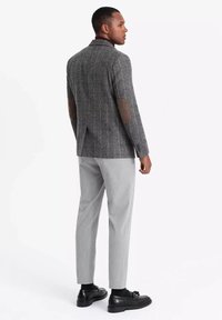 Blazer grigio a righe con toppe marroni sui gomiti, vestibilità sartoriale. Abbinato a pantaloni tapered grigi chiari e scarpe nere. Tessuto testurizzato.