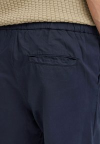 Navy blue pants with a smooth texture and elastic waistband. Features a single back pocket with a rectangular opening.