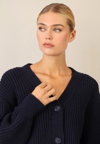 Marineblauer gerippter Strickcardigan mit V-Ausschnitt, der drei große Knöpfe und strukturierte Ärmel aufweist, aus dickem und gemütlichem Stoff.