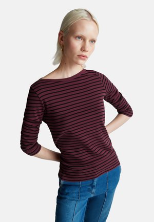 Haut à manches longues rayé en bordeaux et noir, avec un col bateau et une silhouette ajustée, associé à un jean en denim. Texture lisse.
