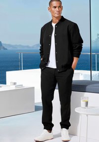 Black bomber jacket with silver snaps, paired with matching black joggers. White t-shirt underneath, complemented by white sneakers.