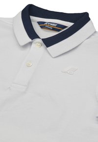 Polo bianca con colletto blu navy, patta con tre bottoni e tessuto texturizzato. Presenta un logo ricamato sul petto.