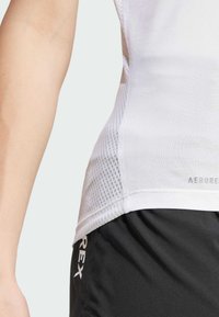 Witte sportieve tanktop met mesh textuur aan de zijkanten, gecombineerd met zwarte shorts met witte branding langs de zoom.
