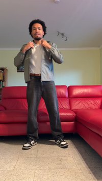 Jasnoszara kurtka na białej koszuli, w połączeniu z ciemnymi dżinsami i czarno-białymi trampkami. W tle czerwona skórzana kanapa.