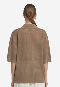 Kortärmad, brun stickad tröja med ett strukturerat mönster, som har en krage och ribbad nederkant. Baksidan visar en öppen stickad design.