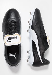Botas de fútbol de cuero negro con un logotipo de Puma en blanco y dorado, que cuentan con una textura suave, punta redondeada y tacos moldeados para tracción.