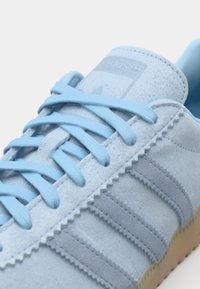 Svetlo modri sueden športni copati z usklajenimi vezalkami in sivimi črtami, ki imajo teksturiran dizajn in gumijast podplat. Standardno blagovno znamko na ježku.