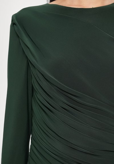 Ciemnozielona sukienka z marszczonym materiałem i poziomym marszczeniem po bokach. Długie rękawy i gładka, miękka faktura.
