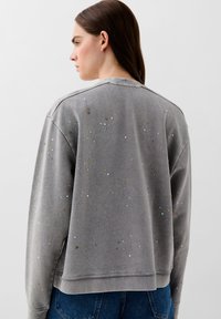 Sudadera gris con cristales de colores dispersos, cuello redondo, puños y dobladillo acanalados. Textura suave con un ajuste relajado.