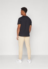 Black cotton t-shirt with short sleeves, paired with light beige tapered joggers and white sneakers, viewed from the back.
