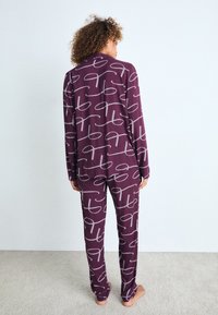 Conjunto de pijama burdeos con un patrón abstracto blanco, hecho de una tela suave, con mangas largas y pantalones, mostrado desde la parte posterior sobre un fondo claro.