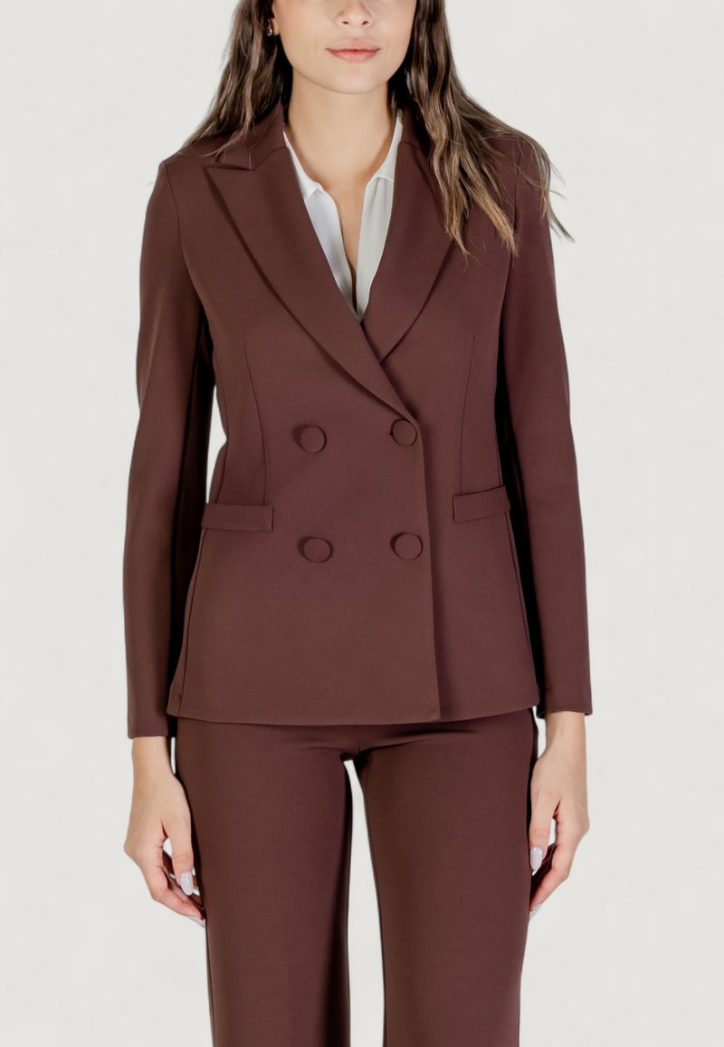 Hnědý dvouřadý blazer vyrobený z hladkého materiálu, s klopami a dvěma předními kapsami, a se šesti odpovídajícími knoflíky. V kombinaci s hnědými kalhotami.