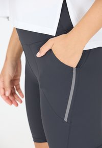 Leggings atletici neri con una tasca laterale, caratterizzati da una trama liscia e una striscia grigia lungo la cucitura della tasca.