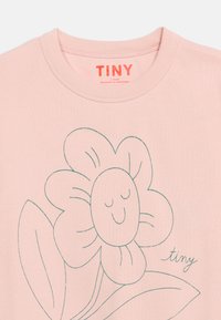 Ελαφρώς ροζ παιδικό πουκάμισο με απλό πράσινο σκίτσο ενός χαμογελαστού λουλουδιού και τ η λέξη "tiny" στο μπροστινό μέρος κάτω από το λαιμό.