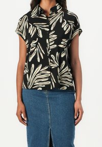 Czarna bluzka z krótkimi rękawami, ozdobiona kremowym wzorem liści i zapinana na guziki. Połączona z dżinsową spódnicą, wyróżniającą się rozcięciem.